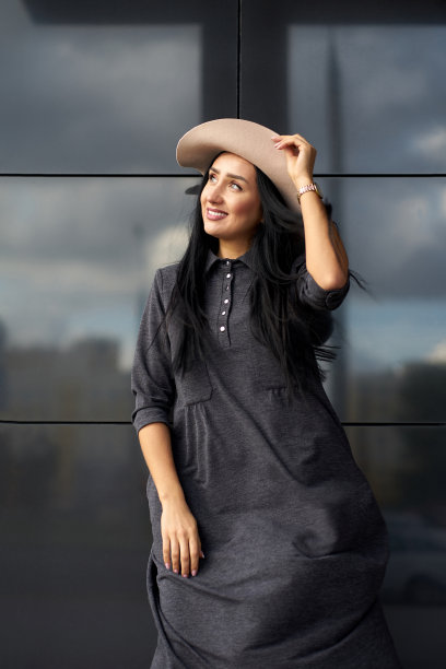 春季潮流女装系列：户外年轻女子，灰色廓形连衣裙与优雅帽子的时尚搭配，都市灰墙背景图片下载