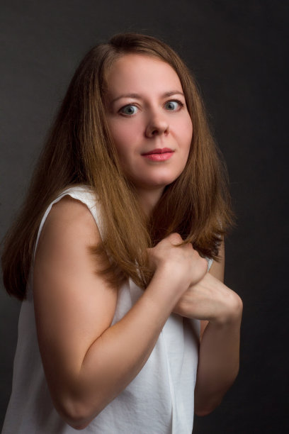 白衬衫黑背景的棕发女孩面露恐惧，姿势拘谨图片下载