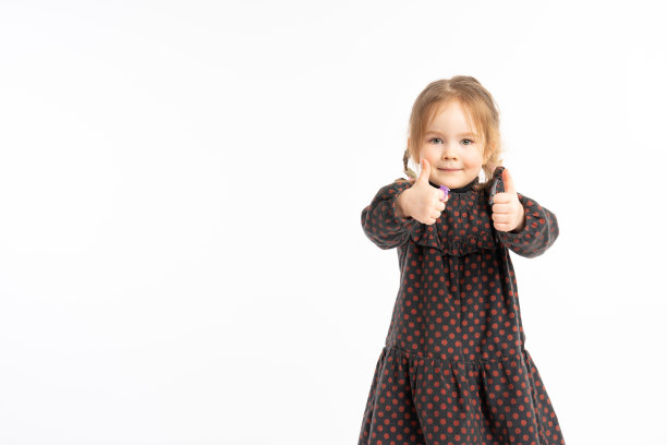 穿着连衣裙的可爱红发小女孩，双手做出积极的姿势，竖起大拇指，面带微笑，非常高兴。看着镜头，带着快乐的表情，做出胜利的手势。图片下载
