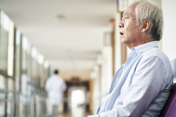一位亚洲老人坐在医院的走廊上，看起来很悲伤和沮丧图片下载