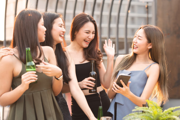 一群年轻美丽快乐的亚洲妇女拿着啤酒与朋友一起聊天，同时庆祝户外屋顶夜总会与广告版面的舞会。图片下载