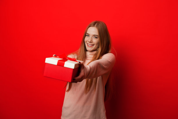 开朗的白人女孩红头发和雀斑是拿着礼物，而摆姿势在红色的背景图片下载