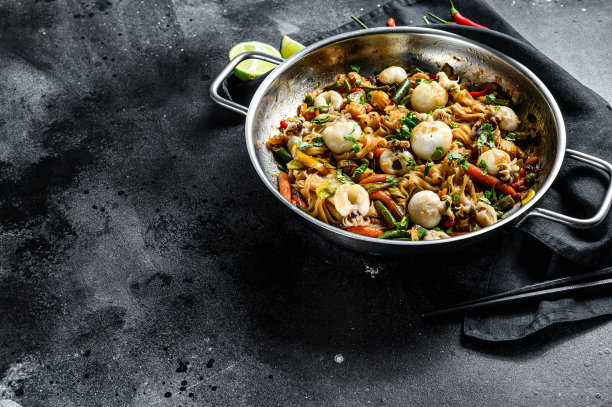 用炒锅炒乌冬面、墨鱼和蔬菜。黑色背景。前视图。本空间图片下载