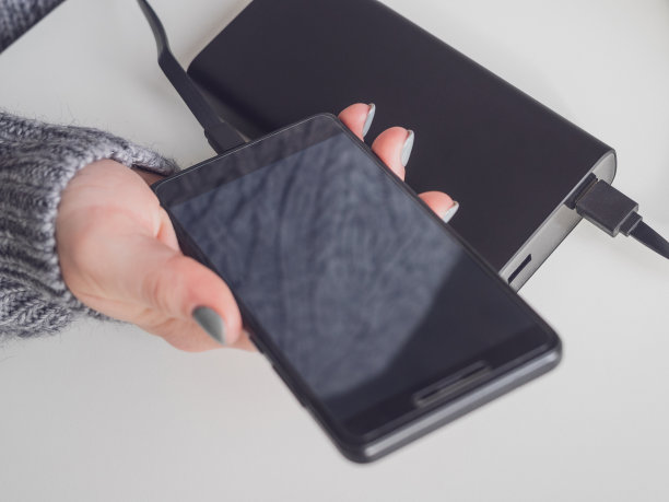 女性手中的手机充电电源。女孩用外接电池给智能手机充电。现代设备和技术，便携式电源。图片下载