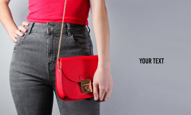 在灰色背景上手拿红色包的穿牛仔裤和T恤的苗条女人，极简主义时尚，留白图片下载