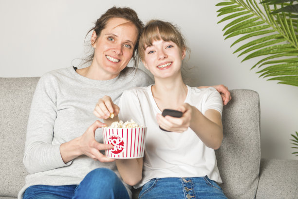 女人和女儿在沙发上看电视吃爆米花的肖像图片下载
