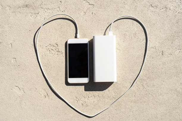 在混凝土背景下为心脏形状的现代智能手机充电。图片下载