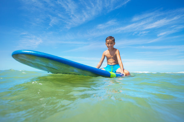 小男孩坐在冲浪板上等待海浪图片下载