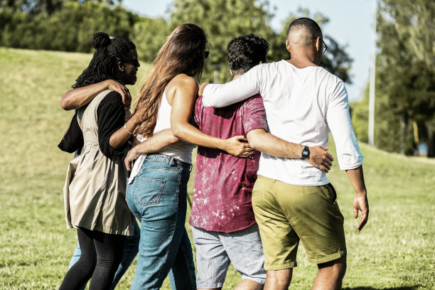 朋友们在草地上散步时拥抱的背影。图片下载