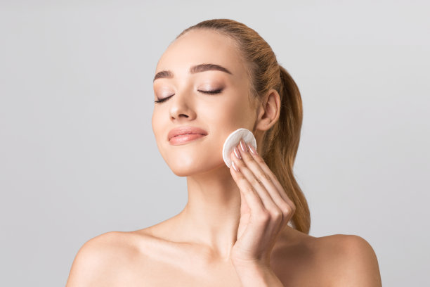 迷人的女孩用化妆棉在灰色的背景上卸妆图片下载