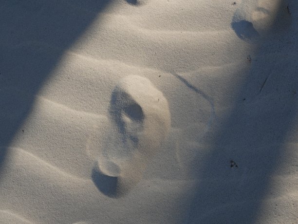 一个人的脚印在一缕阳光洒在沙滩上，躺在傍晚的浪花里。图片下载