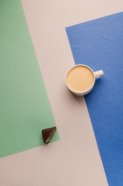 白杯子里的一杯牛奶咖啡，彩色背景是黑巧克力图片下载