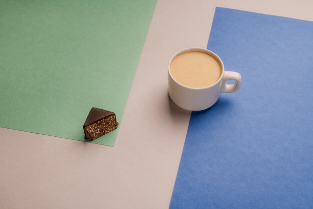 白杯子里的一杯牛奶咖啡，彩色背景是黑巧克力图片下载