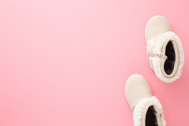 米色皮革温暖婴儿靴子毛绒边浅粉色地板背景。柔和的颜色。文本的空位置。特写镜头。自顶向下的观点。图片下载