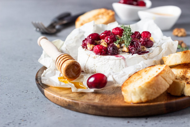 烤卡门培尔奶酪配上蔓越莓、核桃、蜂蜜和百里香，放在羊皮纸上。布里奶酪。灰色石板，石头或混凝土桌。副本的空间。图片下载