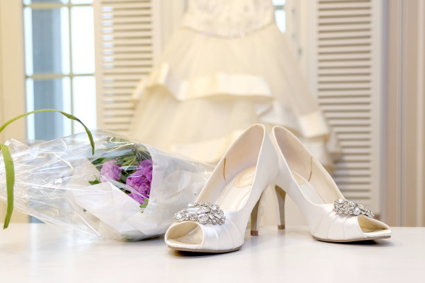 婚礼装饰。白色的婚礼鞋与大高跟鞋和一束花。背景中的婚纱图片下载