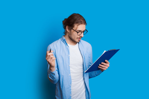 一个留着长胡子的白种人男孩正戴着眼镜看笔记本，在一面蓝色的墙上摆姿势图片下载