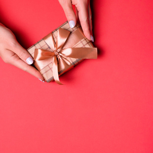女人在红色背景上展示礼品盒，金色心形彩纸。赠送礼物概念，母亲节、妇女节或任何其他节日或庆祝活动的贺卡图片下载