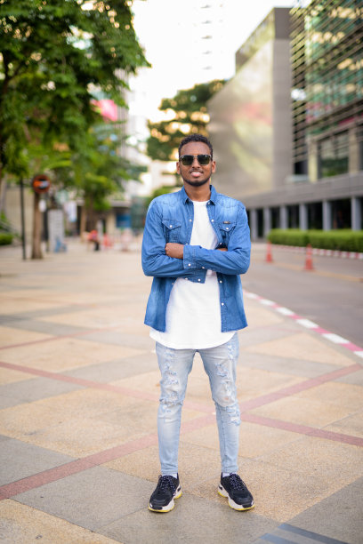 满脸胡须的非洲年轻男子在城市里双臂交叉微笑图片下载
