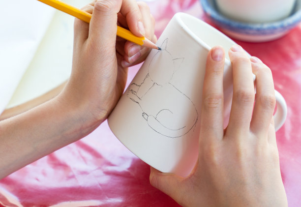 一个孩子在陶艺作坊给一个杯子画画。图片下载