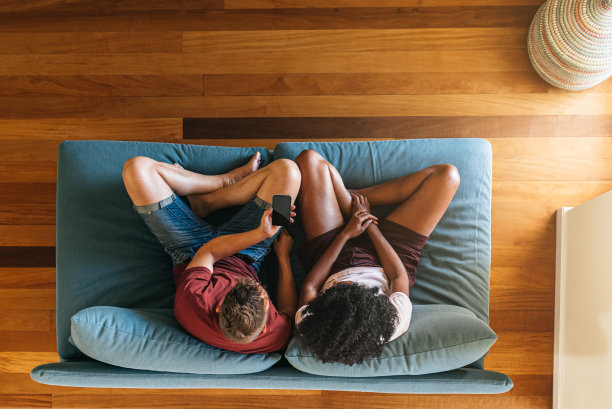 多民族的恋人坐在沙发上，一起玩手机图片下载