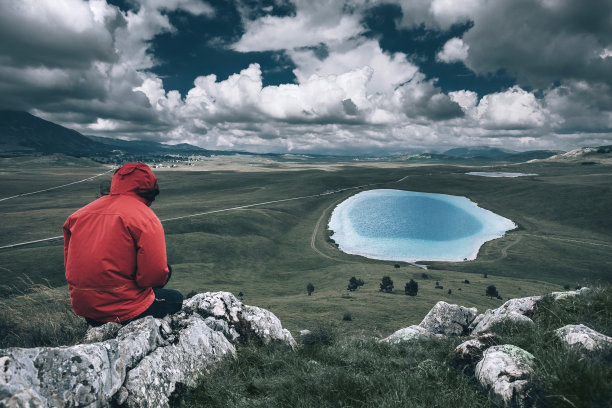 女性穿着运动服坐在山顶上，享受美丽的风景与湖泊图片下载