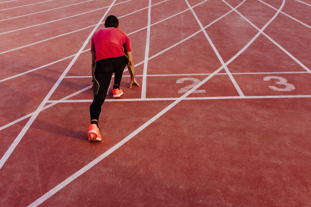 年轻肌肉发达的运动员站在体育场跑道线的起点。体育的概念图片下载