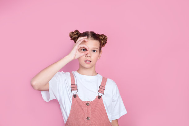 可爱可爱的女孩的肖像在白色t恤女孩做ok的标志在粉红色的背景图片下载