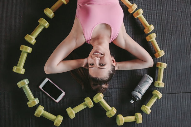 快乐的健身女孩在健身房地板上的哑铃间休息图片下载