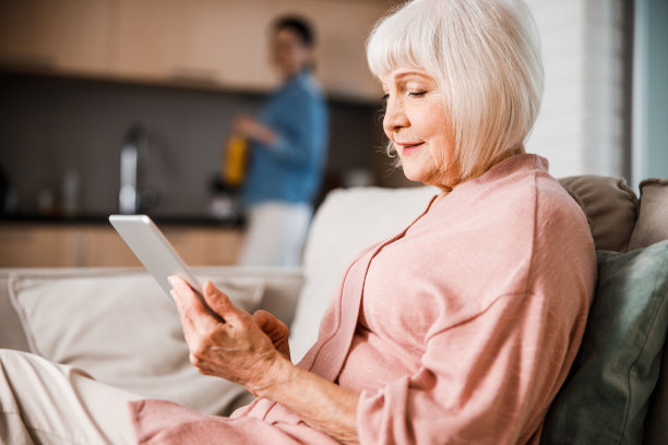 笑容满面的老妇人在家中使用现代电子设备图片下载