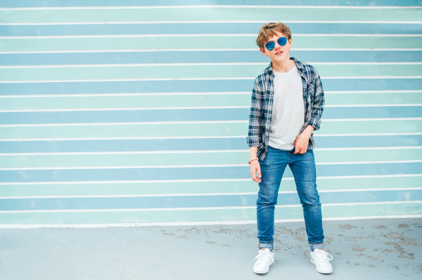 时尚肖像白种人金发12岁的十几岁男孩穿着t恤和格子衬衫在蓝色太阳镜摆姿势在蓝绿色背景墙背景。青少年的时尚概念。图片下载