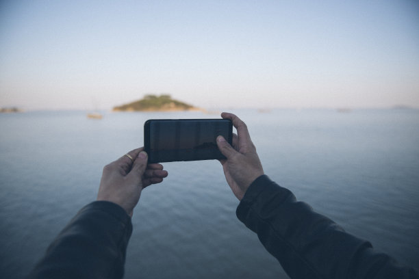 手机上的照片：用智能手机从侧面拍摄的人，晨湖雾气升腾的太阳，平静的早晨氛围，自拍图片下载