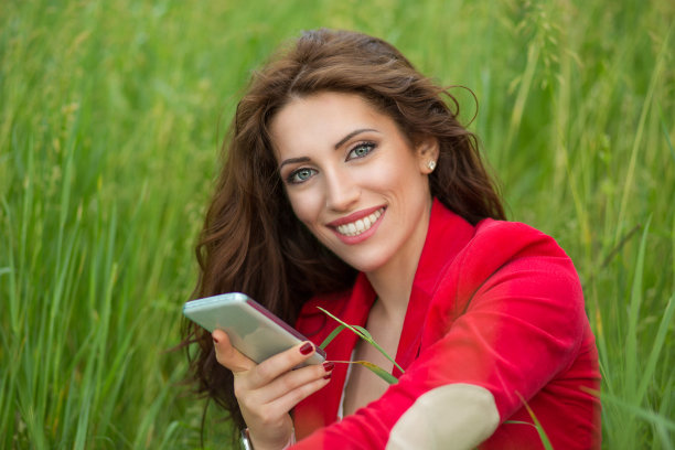 快乐的女人用智能手机微笑，看着你的相机。积极的面部表情图片下载