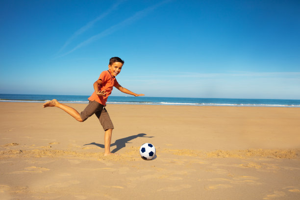 小男孩在沙滩上踢足球图片下载