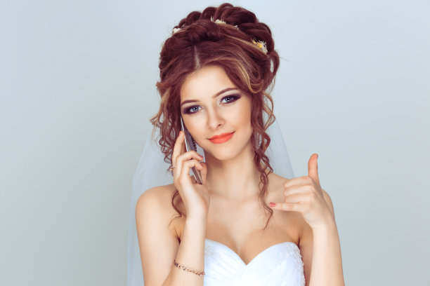 打我的手机。美丽的新娘用手机说话，用手给我打打电话的手势。孤立的浅蓝色白色背景图片下载