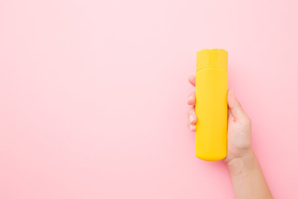 年轻女子展示粉色背景上的黄色防晒霜，特写俯视图图片下载