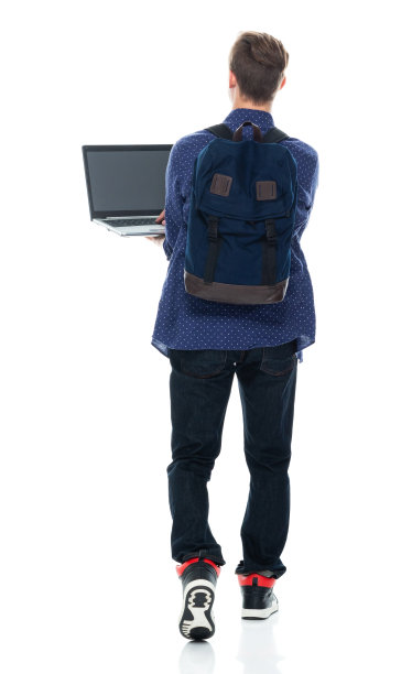 男生背着背包，拿着课本，使用笔记本电脑走在白色背景前图片下载