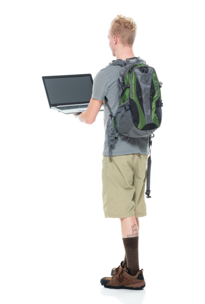白人年轻男性背包客穿着登山靴，拿着包，使用笔记本电脑在白色背景前徒步旅行图片下载