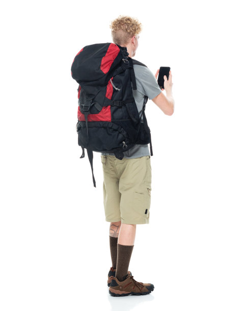 白种年轻男性背包客在白色背景前背着背包，拿着包，使用智能手机图片下载