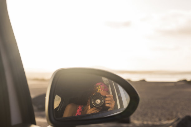 年轻女子从一辆汽车的后视镜拍照。夏天。生活方式图片下载