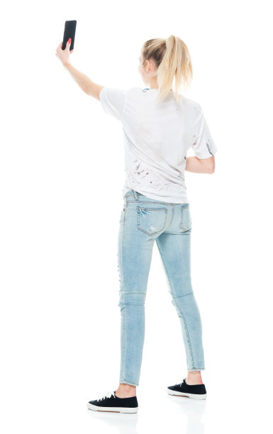 z一代的少女们穿着牛仔裤站在白色背景前用手机拍照图片下载