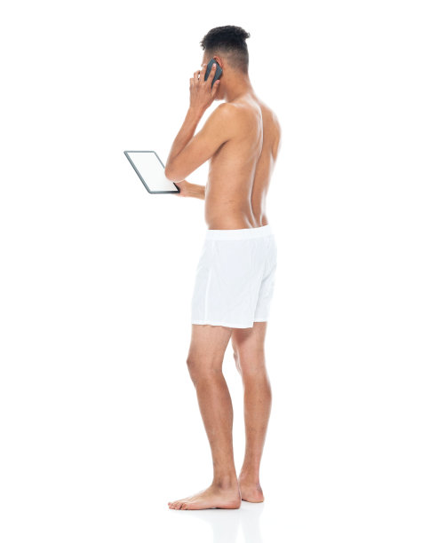 非洲裔男性穿着平角短裤，用着平板电脑站在白色背景前图片下载