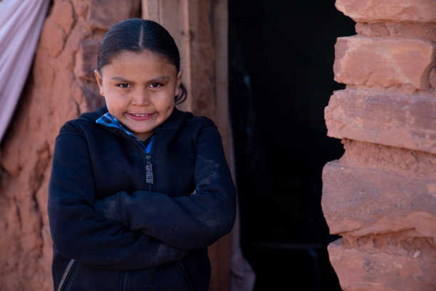 一个年轻的纳瓦霍男孩双手交叉，站在他家人的霍根身边图片下载