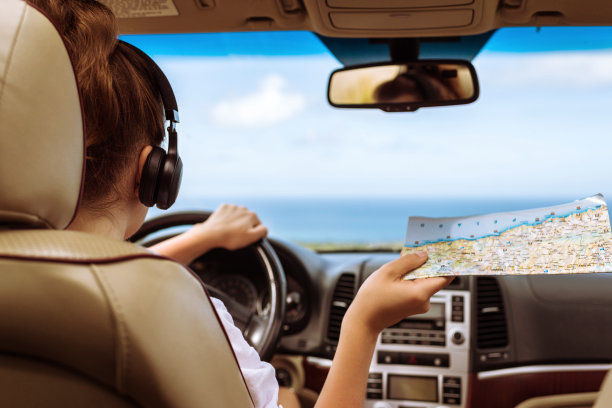 女司机戴着耳机，一边开车一边看地图。女孩放松在自动旅行沿着海洋热带海滩在背景。旅行的概念。图片下载