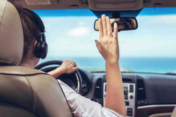 女司机戴着耳机开车。女孩放松在自动旅行沿着海洋热带海滩在背景。旅行的概念。后视图图片下载