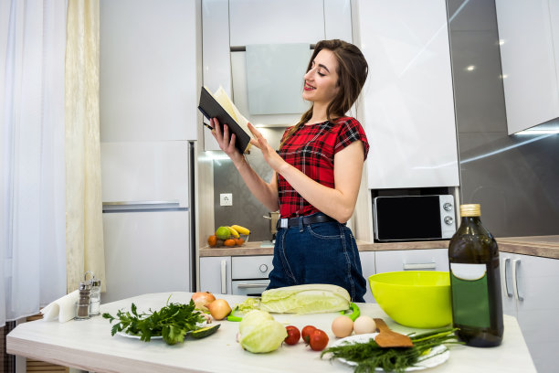 年轻漂亮的女人坐在厨房的桌子上，吃着不同的蔬菜，在日记里写下关于健康营养的每一件事。图片下载