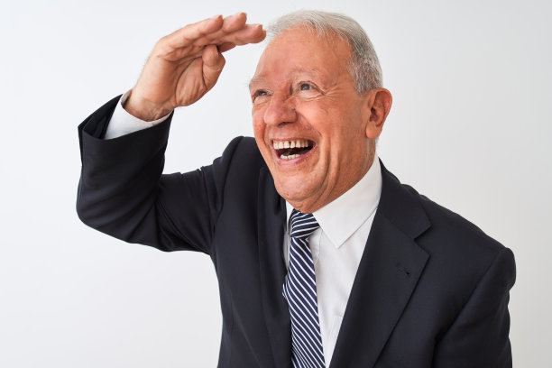 白发苍苍的资深商人穿着西装，站在孤立的白色背景下，非常开心，微笑着把手举过头顶望着远方。搜索概念。图片下载