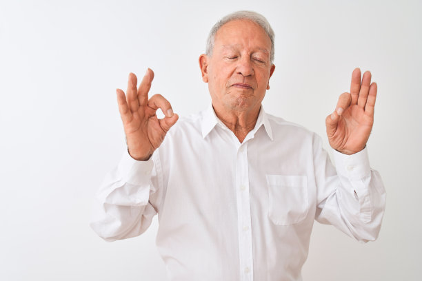 年长的灰白头发男子穿着优雅的衬衫站在孤立的白色背景放松和微笑，闭上眼睛做冥想手势与手指。瑜伽的概念。图片下载