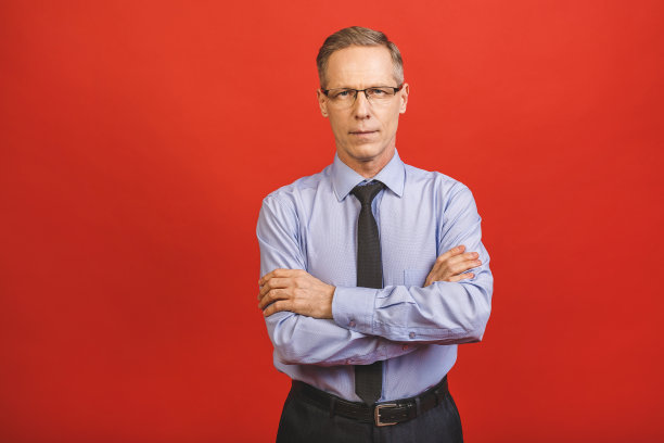 中年老人白发苍苍的老人戴着眼镜越过孤立的红色背景，笑脸相迎，双臂交叉看着镜头。积极的人。图片下载