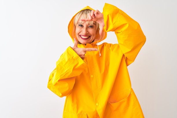 中年妇女穿着雨衣与兜帽站在孤立的白色背景微笑与手和手指框架与快乐的脸。创意和摄影概念。图片下载